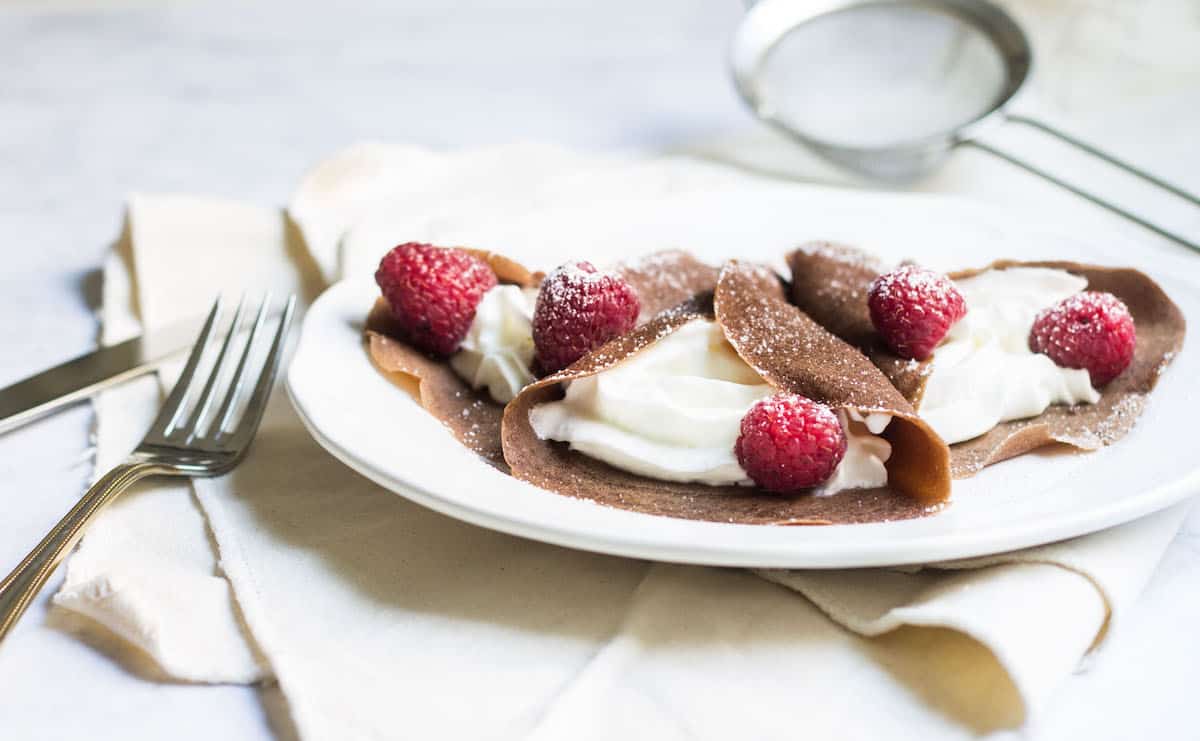 Chocolate Crepes filled with cream and fresh raspberries, then dusted with powdered sugar. So easy and so delicious! Recipe via MonPetitFour.com