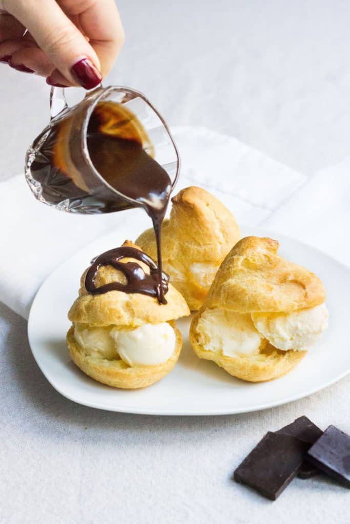 warm chocolate sauce being poured over profiteroles