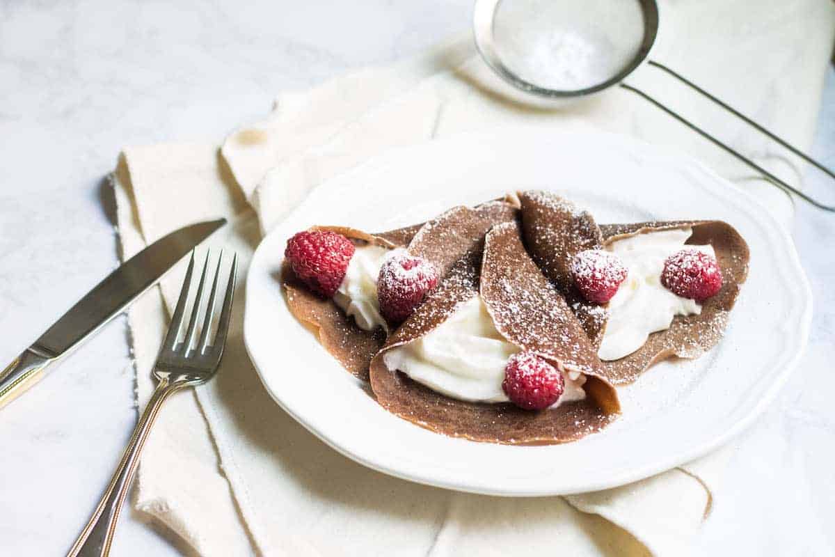 Chocolate Crepes filled with cream and fresh raspberries, then dusted with powdered sugar. So easy and so delicious! Recipe via MonPetitFour.com