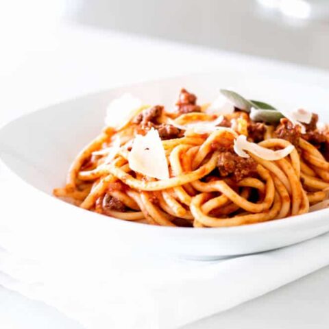 Simple Bolognese Recipe bowl of spaghetti with fresh parmesan shavings and herbs