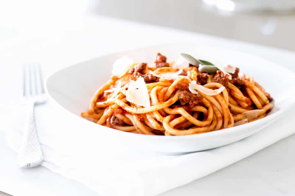 Simple Bolognese Recipe bowl of spaghetti with fresh parmesan shavings and herbs