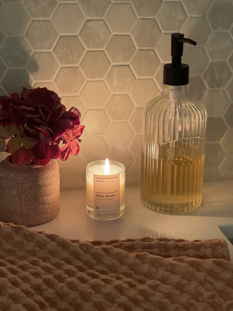 candle and soap dispenser with vase of flowers next to sink