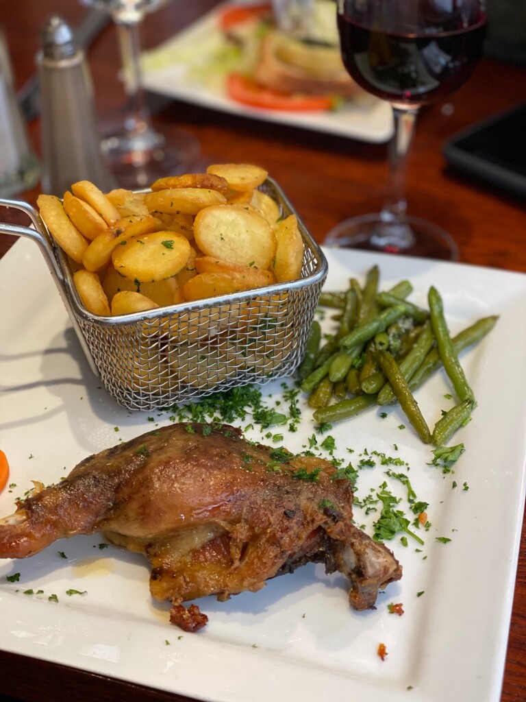 Crispy roast potatoes served in a basket next to duck confit at a French bistro