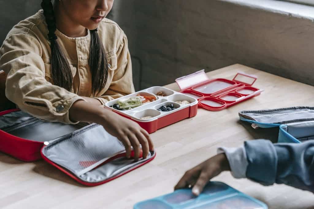 From above of crop anonymous ethnic schoolkids with lunch boxes full of delicious food in classroom