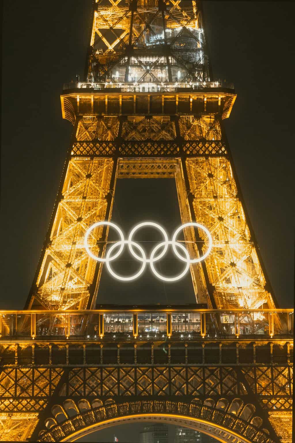 Close-up photograph of the Eiffel Tower in France illuminated at night with the Paris 2024 Olympic rings