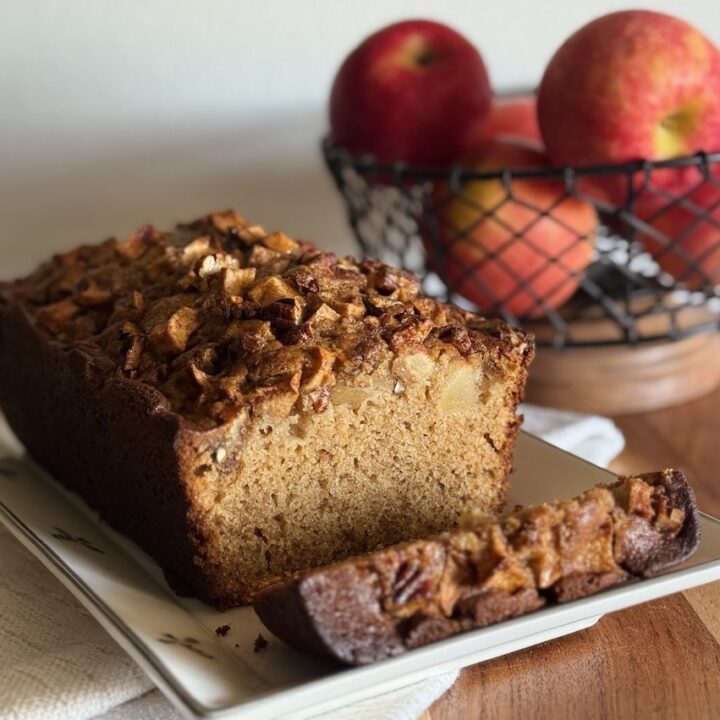 apple cider bread loaf on a dish next to a bowl of apples