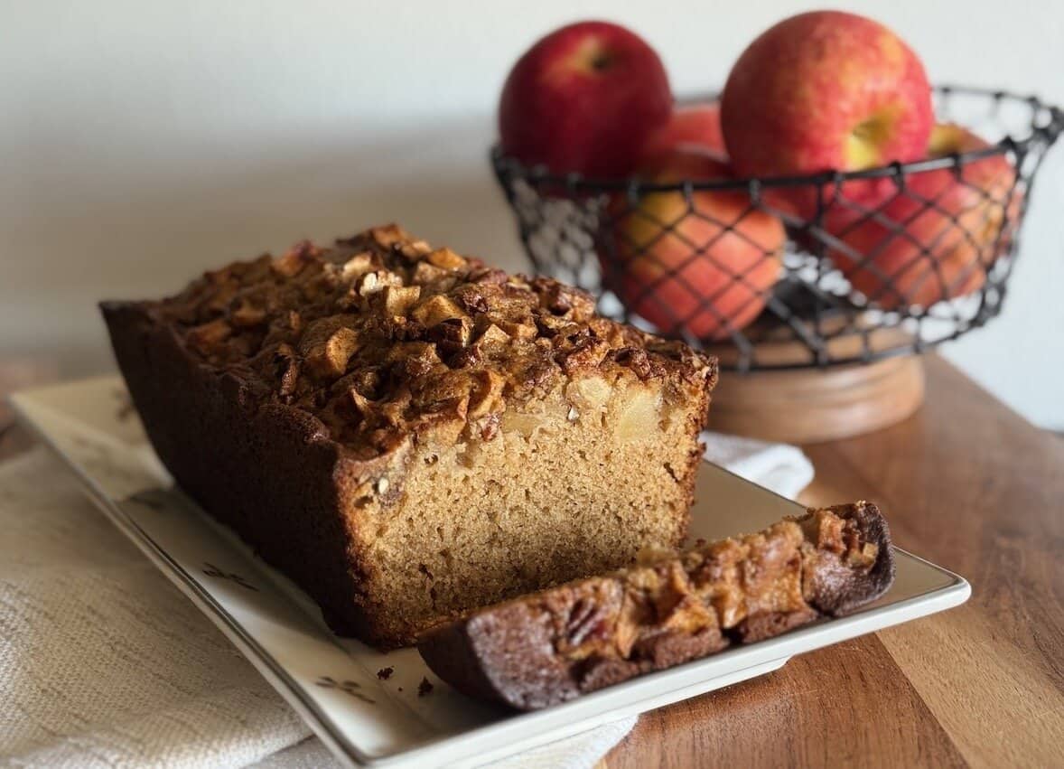 apple cider bread loaf on a dish next to a bowl of apples